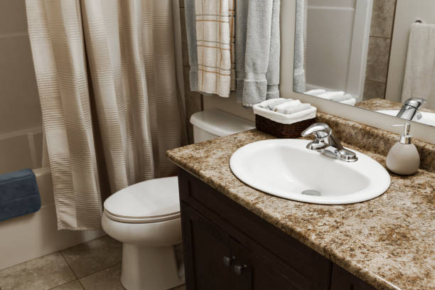 Neatly remodeled small bathroom in Philadelphia featuring a dark wood vanity with granite countertop, undermount sink, chrome faucet, framed mirror, white toilet, and neutral beige tile flooring with a shower curtain enclosure.