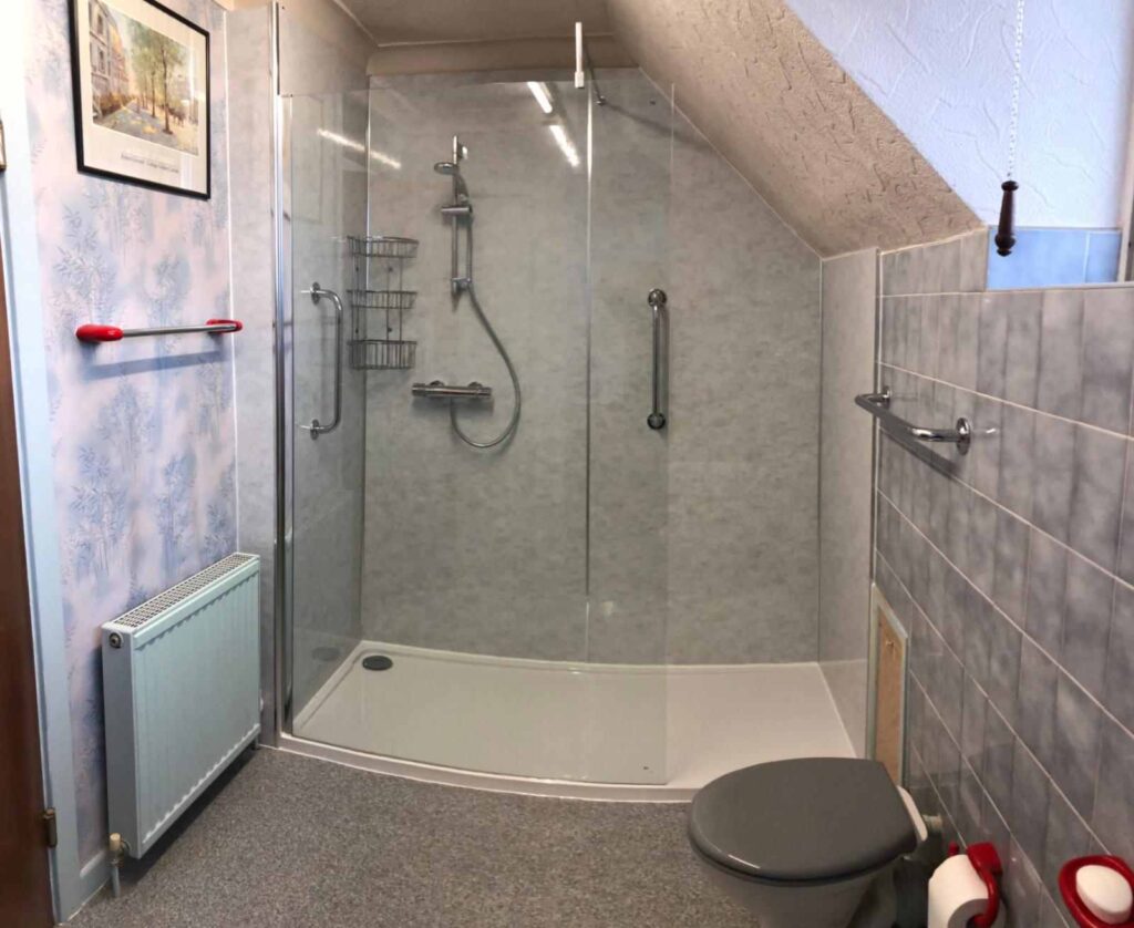 Completed walk-in shower installation in Philadelphia featuring a curved frameless glass enclosure with gray stone panel walls, chrome grab bars, handheld shower system, and a low-entry shower tray designed for accessibility and comfort.